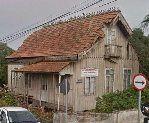 Casa com lambrequim na beira do telhado, varanda em uma das laterais e sacada na parte superior.